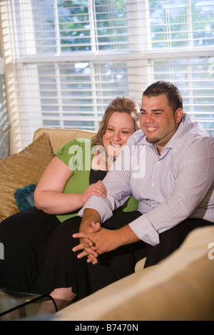 Happy overweight couple sitting on sofa in living room Stock Photo