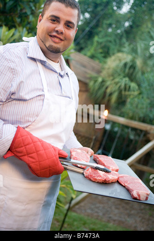 Smiling man holding steaks on forks in hands. Happy male ready to eat ...