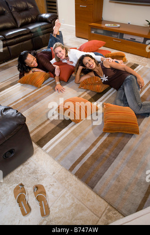 Three happy multi-ethnic women lying on carpet in living room, high angle view Stock Photo
