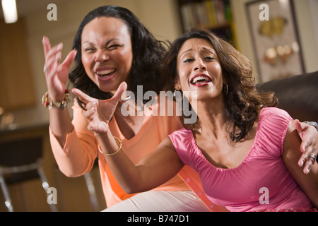 Two laughing multi-ethnic women sitting in living room Stock Photo