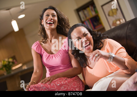 Two laughing multi-ethnic women sitting in living room Stock Photo