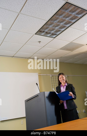 Young Asian woman reading file by lectern in board room Stock Photo