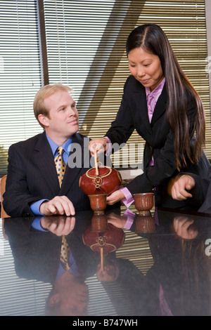 Young Asian woman serving tea to Caucasian businessman in boardroom Stock Photo
