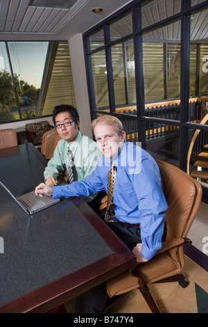 Two multi-ethnic businessmen sitting with laptop in boardroom Stock Photo