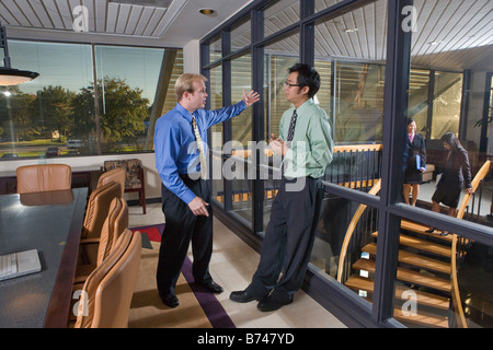 Businessmen talking in boardroom, women on stairs in background Stock Photo