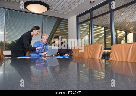 Three multi-ethnic businesspeople working on laptop in boardroom Stock Photo