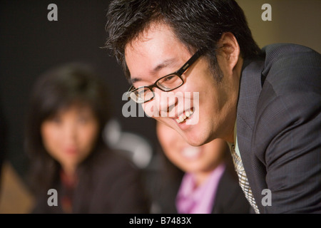 Three Asian businesspeople talking in boardroom, focus on foreground Stock Photo