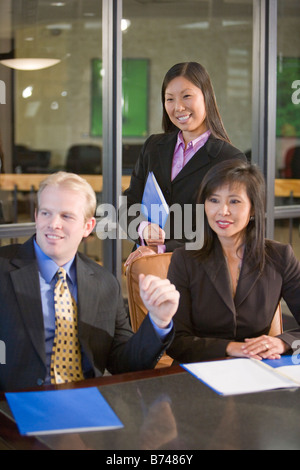 Three multi-ethnic businesspeople sitting with files in boardroom, smiling Stock Photo