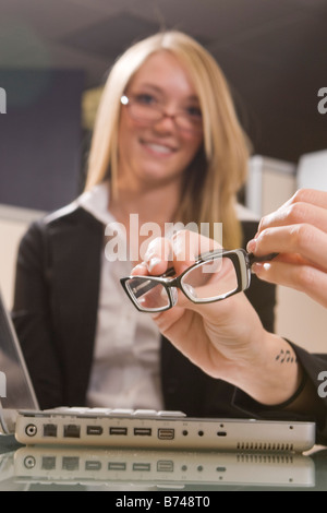 Hands holding eyeglasses, female office worker in background Stock Photo