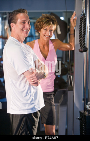Middle-aged couple using weight machine at gym Stock Photo