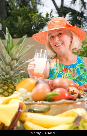 Mature woman drinking lemonade, surrounded by tropical fruit Stock Photo