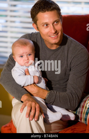 Father holding baby boy while sitting on sofa Stock Photo