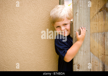 Young boy peeking through wooden door Stock Photo