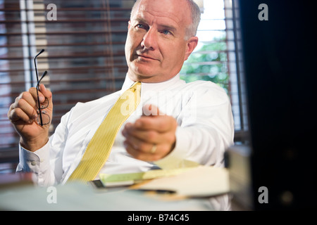 Businessman sitting in office holding glasses with window in background Stock Photo