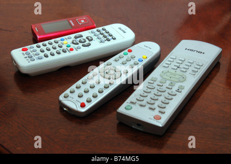 A red mobile phone lies on a table alongside remote controls for digital T.V, DVD. Stock Photo