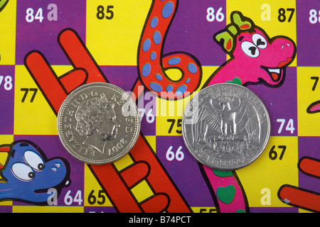 one us quarter dollar 25c coin and pound coin on a snakes and ladders board with pound on the ladder and quarter on the snake Stock Photo