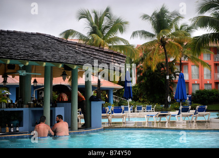TWO TOURISTS SIT AT THE POOL BAR DURING A RAIN STORM AT A CARIBBEAN HOLIDAY RESORT Stock Photo