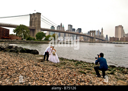 Wedding Couple being photographed by Brooklyn Bridge in New York with Manhattan skyline in background Stock Photo