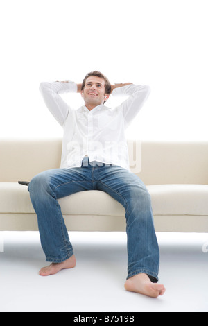 One mid adult man sitting on sofa with hands behind head Stock Photo