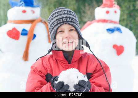 Ten year old boy holding snow, beside snowmen, Winnipeg, Canada Stock Photo