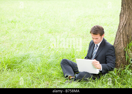 One mid adult man leaning against tree using laptop Stock Photo