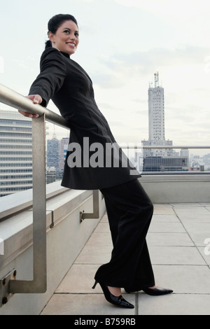 Side profile of a businesswoman leaning against a railing and smiling Stock Photo