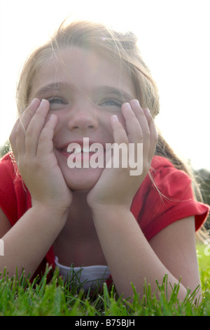 Six year old girl with chin in hands lying on grass, Winnipeg, Manitoba, Canada Stock Photo