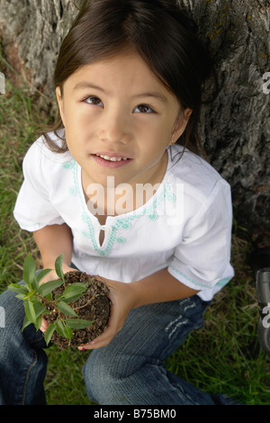 Six year old girl holding small tree, looking upward, Winnipeg, Canada Stock Photo