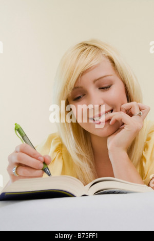 Low angle view of a young woman lying on the bed and writing with a pen in a book Stock Photo