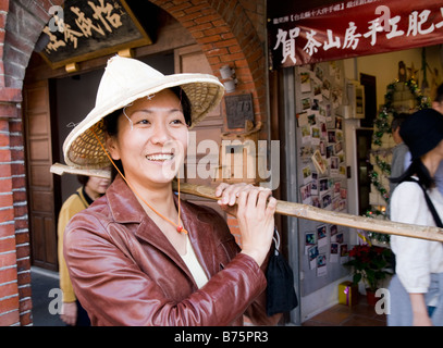 oriental beautiful girl in traditional straw hat carrying pole on her shoulder Stock Photo