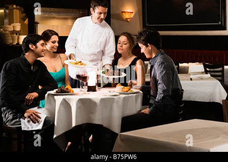 Male chef serving food to two young couples sitting in a restaurant Stock Photo