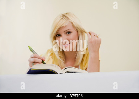 Low angle view of a young woman lying on the bed and writing with a pen in a book Stock Photo