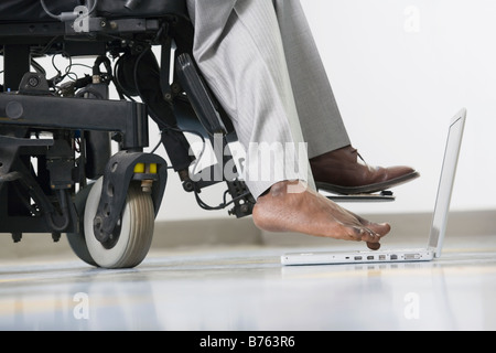 Low section view of a businessman with Cerebral Palsy sitting in a wheelchair and working on a laptop with his foot Stock Photo