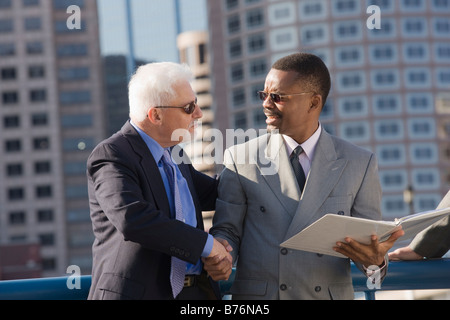 Two businessmen shaking hands on bridge Stock Photo