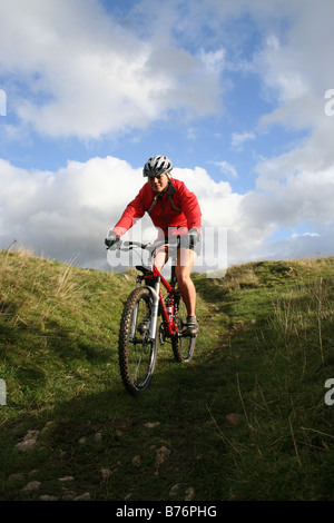 Young female mountain biker descending into Long Dale in the Derbyshire Dales of the Peak District Stock Photo