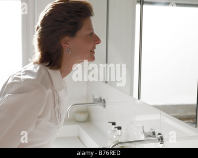 Mature woman looking into the mirror in the bathroom smiling Stock Photo