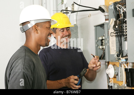 Two electricians working on an electrical panel together Actual electricians performing work according to industry codes Stock Photo