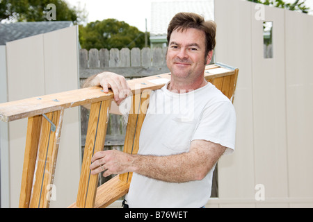 Friendly handyman carrying a ladder and smiling Stock Photo