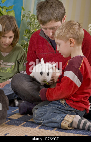 father sits with his children on the floor and plays with domestic rabbit Stock Photo