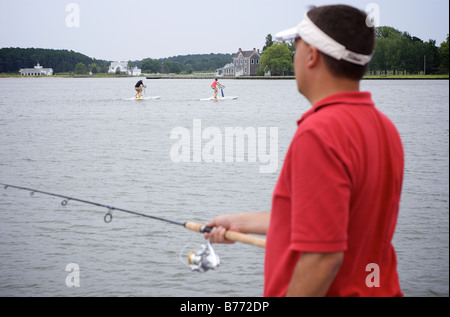 Man in red shirt fishing with two water bikers in background at Chesapeake Bay Maryland Stock Photo