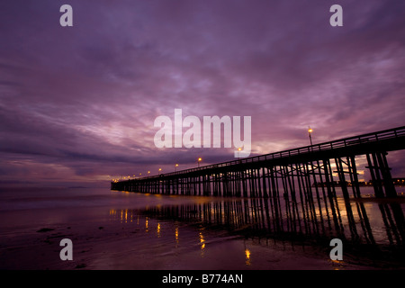 A pier and the ocean at low tide during sunset. Stock Photo