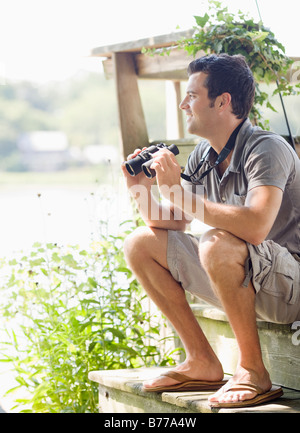 Man sitting on steps of deck binoculars Stock Photo