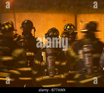 Firefighters standing outside burning building Stock Photo