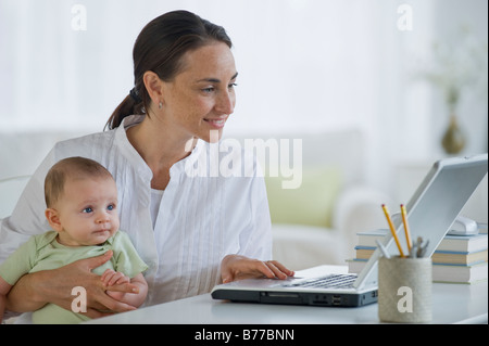 Mother working on laptop and holding baby son Stock Photo