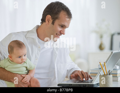 Father working on laptop and holding son Stock Photo