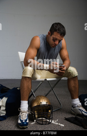 Football player looking cell phone locker room Stock Photo