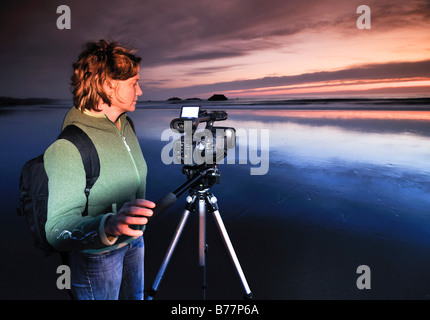 Camerawoman with movie camera filming sunset with a tripod at Meyers Creek Beach, Pistol River State Park, Oregon Coast, Oregon Stock Photo