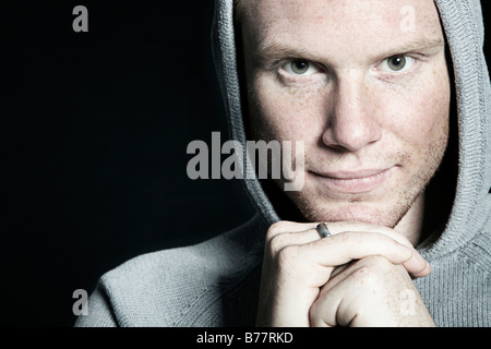 Portrait of a young man wearing a hooded sweatshirt resting his head on his hands Stock Photo