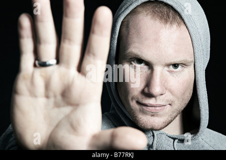Portrait of a young man wearing a hooded sweatshirt, protectively holding out a hand Stock Photo