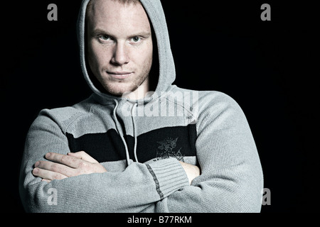 Portrait of a young man wearing a hooded sweatshirt, crossing his arms Stock Photo